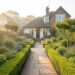 Jardin soigné autour d’une maison, allées bien tracées et massifs taillés, ambiance lumineuse naturelle et douce.