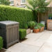 Jardin urbain soigneusement entretenu avec composteur fermé, haies taillées et rangement extérieur bien ordonné sous une lumière naturelle.